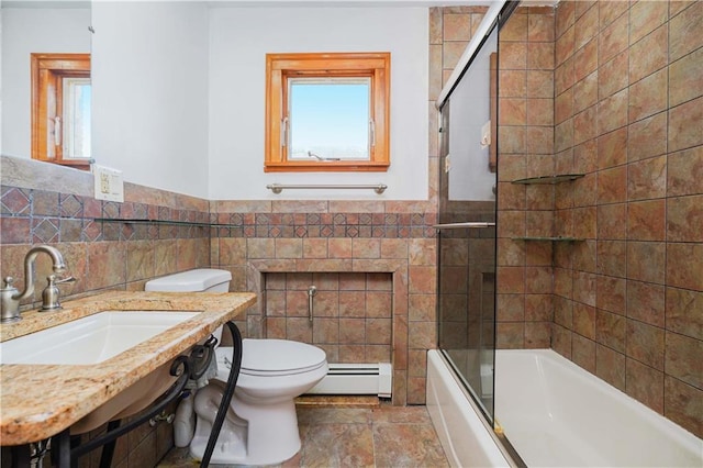 full bathroom with toilet, tile walls, bath / shower combo with glass door, a baseboard heating unit, and sink