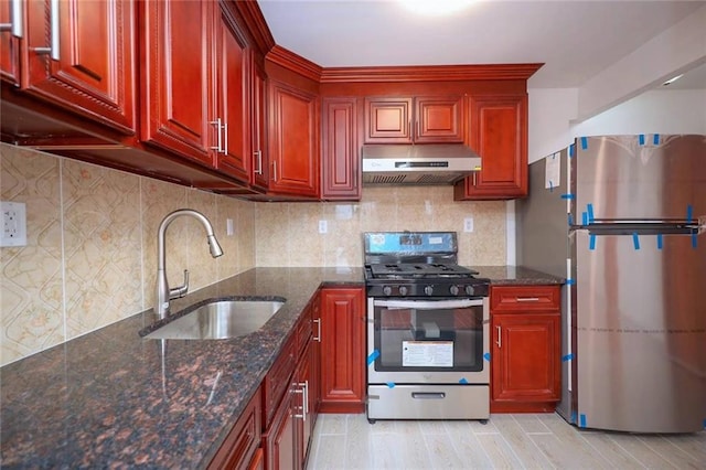 kitchen with sink, light wood-type flooring, stainless steel appliances, dark stone countertops, and decorative backsplash