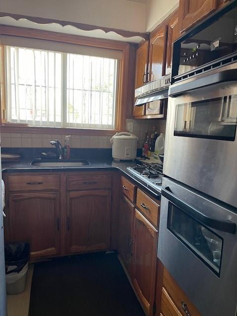 kitchen featuring a sink, decorative backsplash, appliances with stainless steel finishes, and brown cabinetry