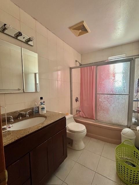 full bathroom with tile walls, tiled shower / bath combo, vanity, toilet, and tile patterned floors