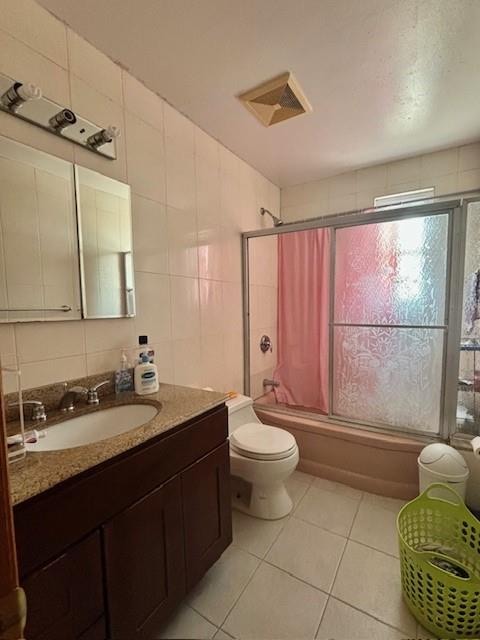 full bath with tile patterned floors, bath / shower combo with glass door, toilet, tile walls, and vanity