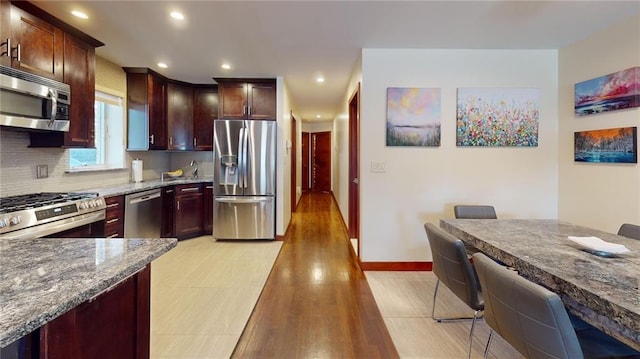 kitchen with dark stone counters, light hardwood / wood-style flooring, tasteful backsplash, a kitchen bar, and stainless steel appliances