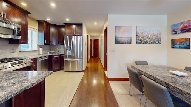 kitchen featuring recessed lighting, stainless steel appliances, dark stone countertops, backsplash, and light wood-style flooring