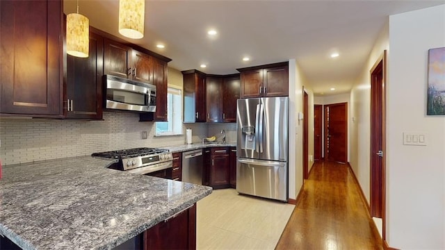 kitchen featuring pendant lighting, light wood-type flooring, kitchen peninsula, and appliances with stainless steel finishes