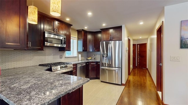kitchen with stainless steel appliances, a peninsula, dark stone countertops, and tasteful backsplash