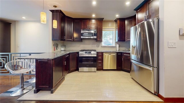 kitchen with kitchen peninsula, appliances with stainless steel finishes, light stone counters, a breakfast bar, and pendant lighting