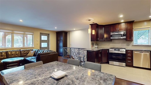 kitchen with decorative light fixtures, a wealth of natural light, light stone countertops, and appliances with stainless steel finishes