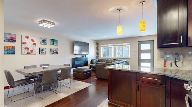 kitchen with hanging light fixtures, wood finished floors, open floor plan, a peninsula, and light stone countertops