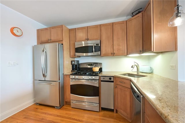 kitchen with pendant lighting, sink, stainless steel appliances, light stone countertops, and light hardwood / wood-style flooring