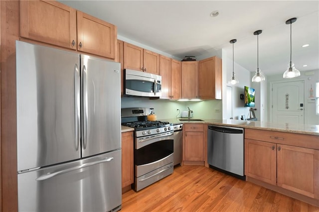 kitchen with decorative light fixtures, sink, stainless steel appliances, light stone countertops, and light wood-type flooring