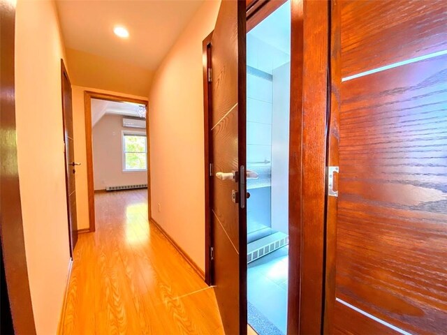 hallway with a wall unit AC, lofted ceiling, and light hardwood / wood-style flooring