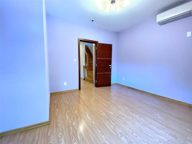 empty room with a notable chandelier, a wall mounted AC, and light wood-type flooring