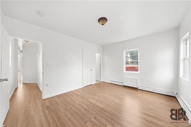 spare room featuring baseboard heating and light hardwood / wood-style flooring