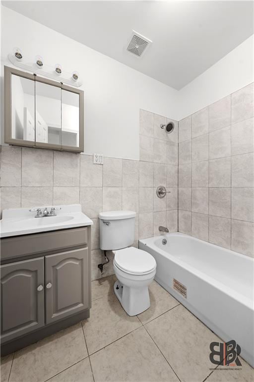 full bathroom with tiled shower / bath combo, tile patterned floors, vanity, tile walls, and toilet