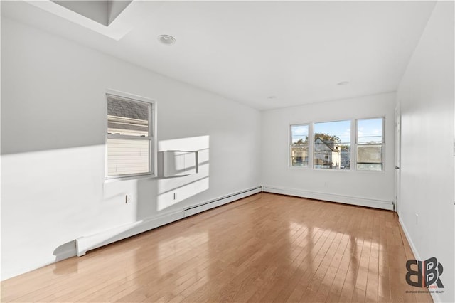 unfurnished room featuring a baseboard radiator, a wealth of natural light, and light wood-type flooring