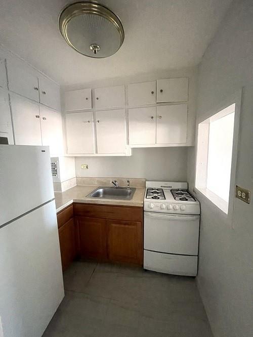 kitchen featuring white appliances, light tile patterned floors, sink, and white cabinets