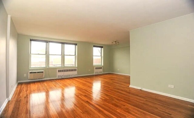 empty room featuring radiator, wood-type flooring, and an AC wall unit