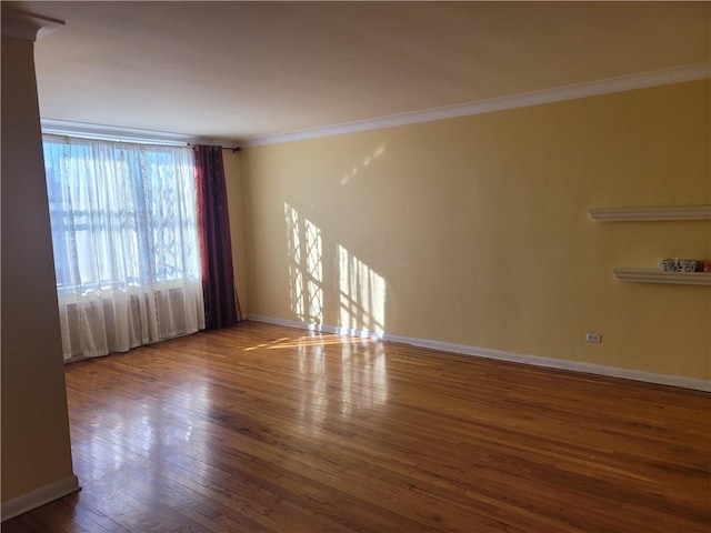 empty room featuring crown molding, baseboards, and wood finished floors