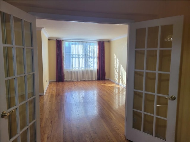 empty room featuring french doors, baseboards, wood finished floors, and crown molding