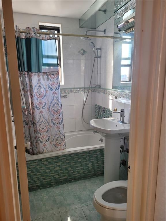 bathroom with tile patterned flooring, toilet, tiled shower / bath combo, and a sink