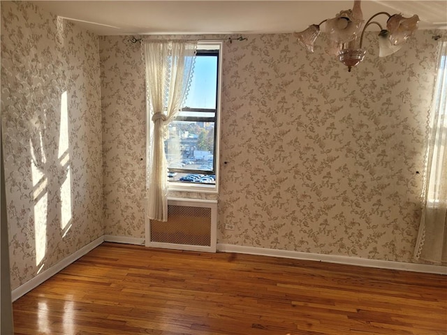 unfurnished room featuring baseboards, hardwood / wood-style flooring, radiator heating unit, and wallpapered walls