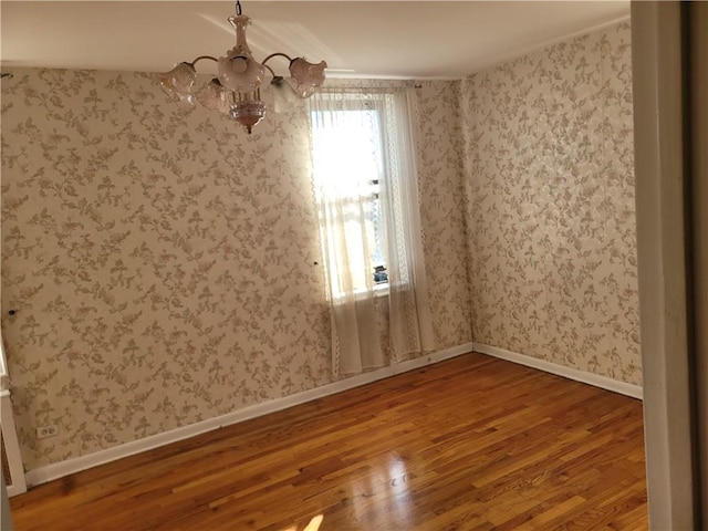 unfurnished room featuring a notable chandelier, wallpapered walls, baseboards, and wood finished floors