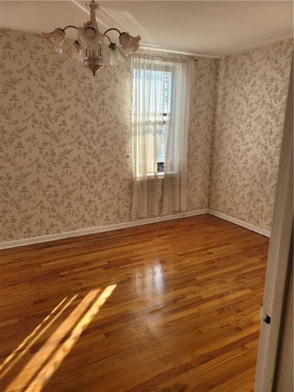 unfurnished room with baseboards, wood finished floors, and wallpapered walls