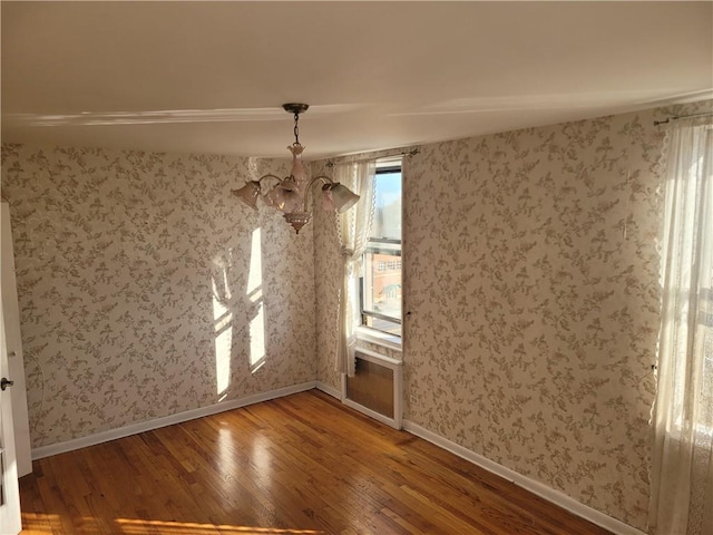 unfurnished dining area featuring baseboards, wallpapered walls, an inviting chandelier, and wood finished floors