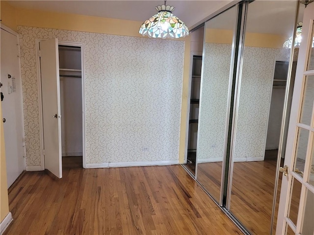 unfurnished bedroom with two closets, wallpapered walls, baseboards, and wood finished floors