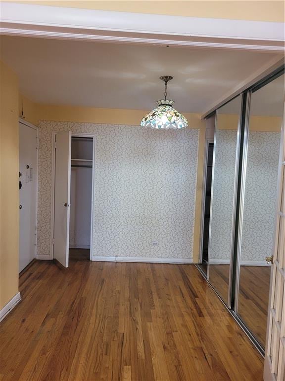 unfurnished dining area with wallpapered walls, wood finished floors, and baseboards