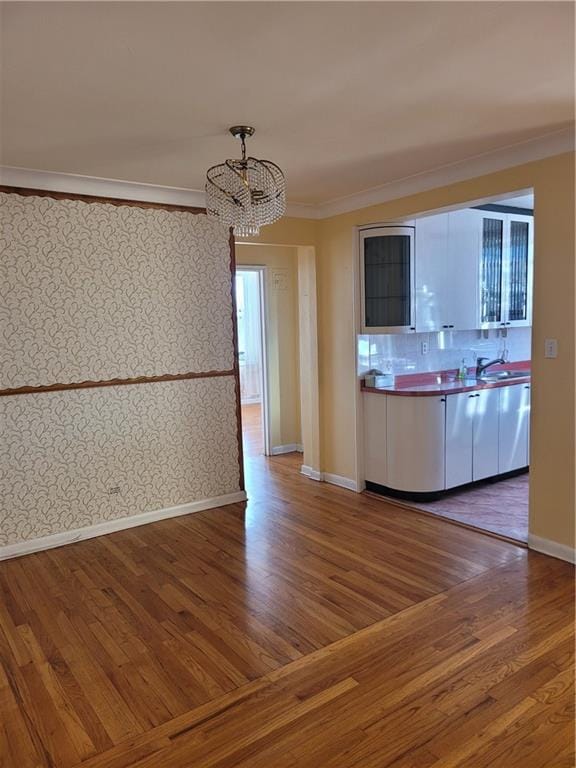 kitchen with wallpapered walls, crown molding, baseboards, an inviting chandelier, and wood finished floors