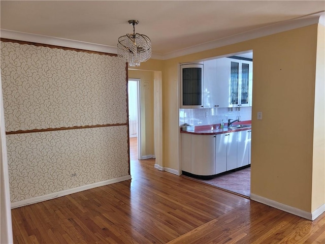 kitchen with baseboards, a chandelier, ornamental molding, wood finished floors, and a sink