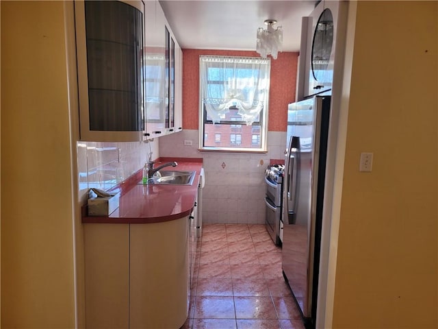 kitchen featuring a sink, stainless steel appliances, tile walls, light tile patterned flooring, and glass insert cabinets