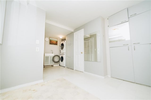 empty room featuring stacked washer and dryer, light floors, and baseboards