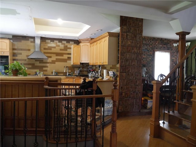 kitchen featuring wall chimney exhaust hood, light brown cabinetry, sink, ornate columns, and wood-type flooring