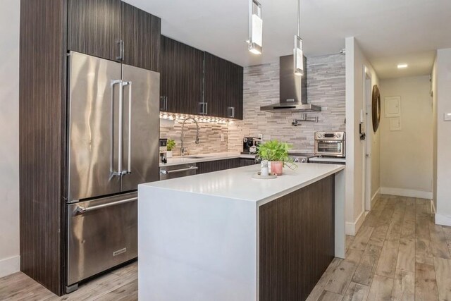 kitchen featuring pendant lighting, sink, appliances with stainless steel finishes, a center island, and wall chimney exhaust hood