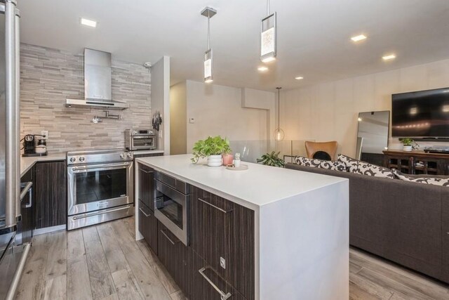 kitchen featuring stainless steel appliances, a center island, light hardwood / wood-style floors, decorative light fixtures, and wall chimney exhaust hood