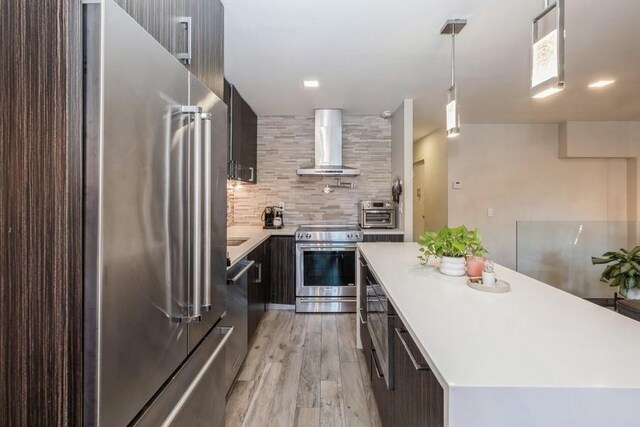 kitchen featuring stainless steel appliances, a kitchen island, decorative light fixtures, wall chimney exhaust hood, and light wood-type flooring