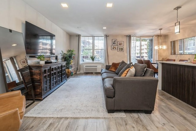 living room with an AC wall unit, an inviting chandelier, and light hardwood / wood-style floors