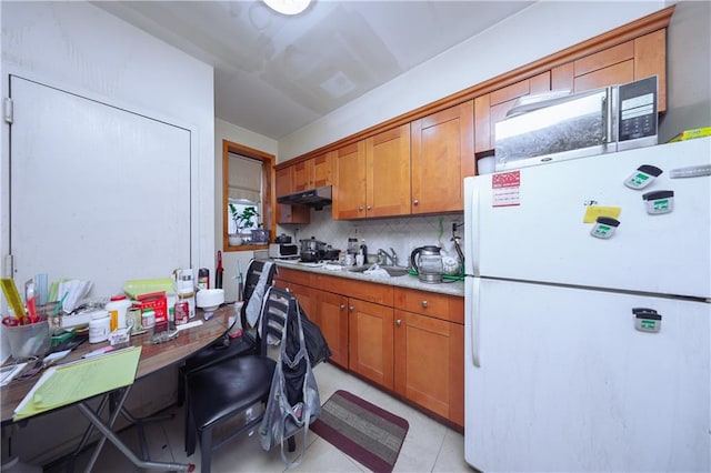 kitchen featuring brown cabinetry, freestanding refrigerator, under cabinet range hood, and light countertops