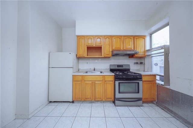 kitchen with sink, light tile patterned flooring, stainless steel range with gas stovetop, white fridge, and tasteful backsplash