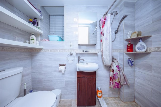 bathroom featuring vanity, tiled shower, toilet, and tile walls