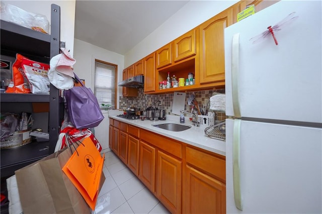 kitchen featuring decorative backsplash, a sink, light countertops, freestanding refrigerator, and under cabinet range hood