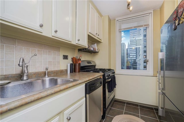 kitchen with appliances with stainless steel finishes, backsplash, dark tile patterned floors, sink, and white cabinetry