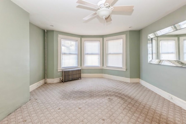 carpeted empty room featuring radiator, ceiling fan, and a skylight