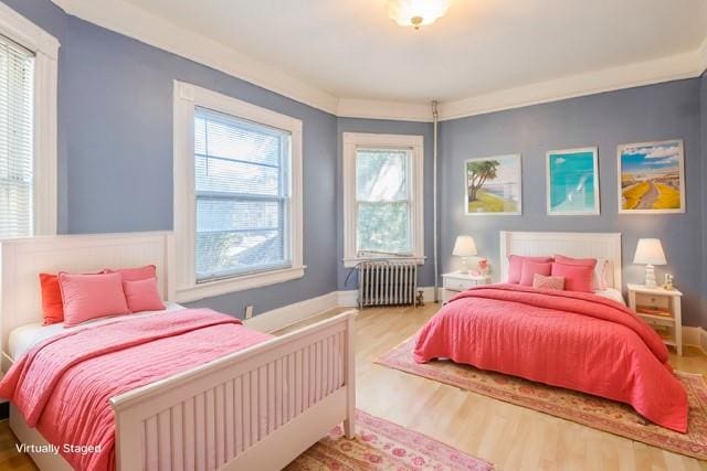 bedroom with light hardwood / wood-style flooring, radiator heating unit, and multiple windows