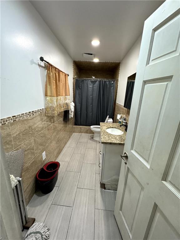 bathroom with vanity, toilet, tile walls, and curtained shower