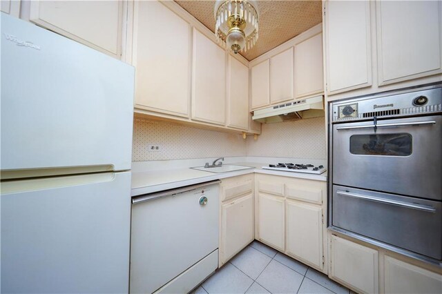 kitchen with white appliances, sink, tasteful backsplash, light tile patterned flooring, and white cabinetry