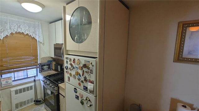 kitchen featuring white fridge, white cabinetry, gas range oven, and radiator heating unit