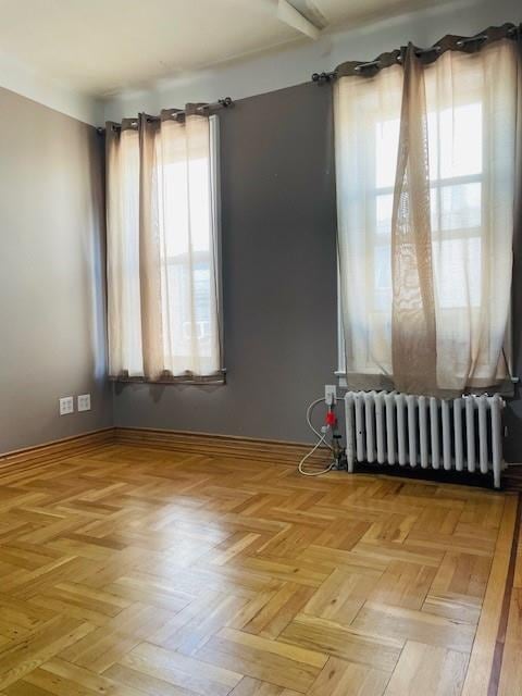 empty room with a healthy amount of sunlight, radiator heating unit, and light parquet flooring